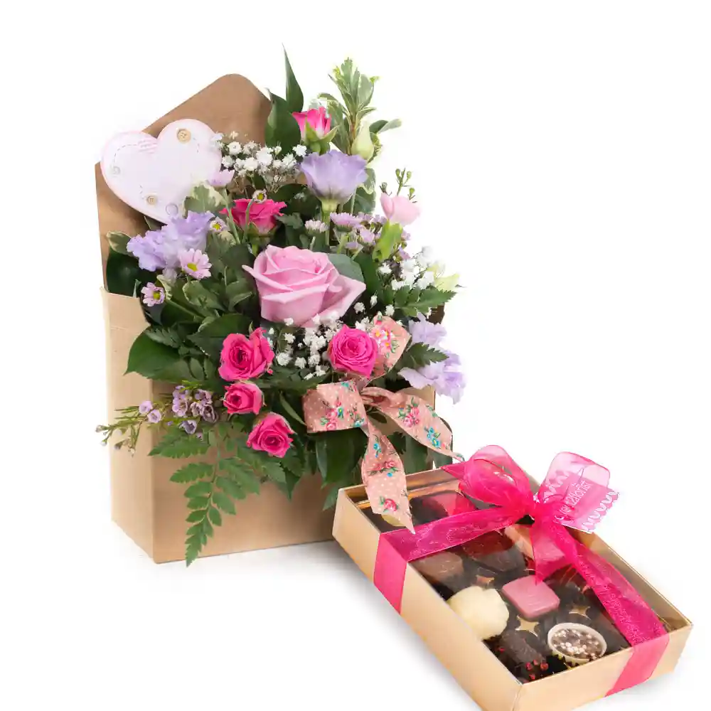 A beautiful Mother's Day bouquet featuring soft pink roses, delicate purple lisianthus, tiny white Gypsophila, and lush green foliage, all arranged in a charming kraft paper envelope. The bouquet is accented with a decorative ribbon and a heart-shaped embellishment. Accompanying the flowers is a box of gourmet chocolates wrapped in a pink ribbon, creating a thoughtful and elegant gift