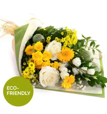 A bouquet of fresh yellow and white flowers, including roses, daisies, and greenery, wrapped in eco-friendly packaging with natural raffia ties. The bouquet has a bright and cheerful appearance, with a mix of delicate blooms and lush foliage.