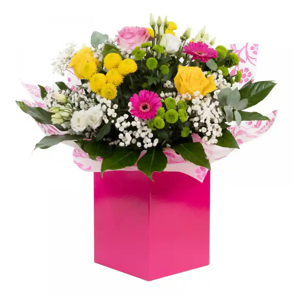 A vibrant mixed flower bouquet in a bright pink gift box, featuring yellow roses, pink gerberas, white lisianthus, green chrysanthemums, and delicate gypsophila.