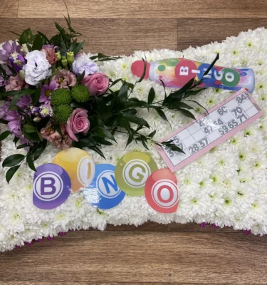 Celebrate cherished memories with our exquisite Bingo Funeral Pillow Tribute from Sun Florist and Events. This personalized tribute adds a heartfelt touch to any memorial service, honoring your loved one's legacy with style and compassion. Explore our beautiful range of funeral florals and custom tributes to ensure a fitting farewell. Contact us today to learn more about our meaningful memorial options.